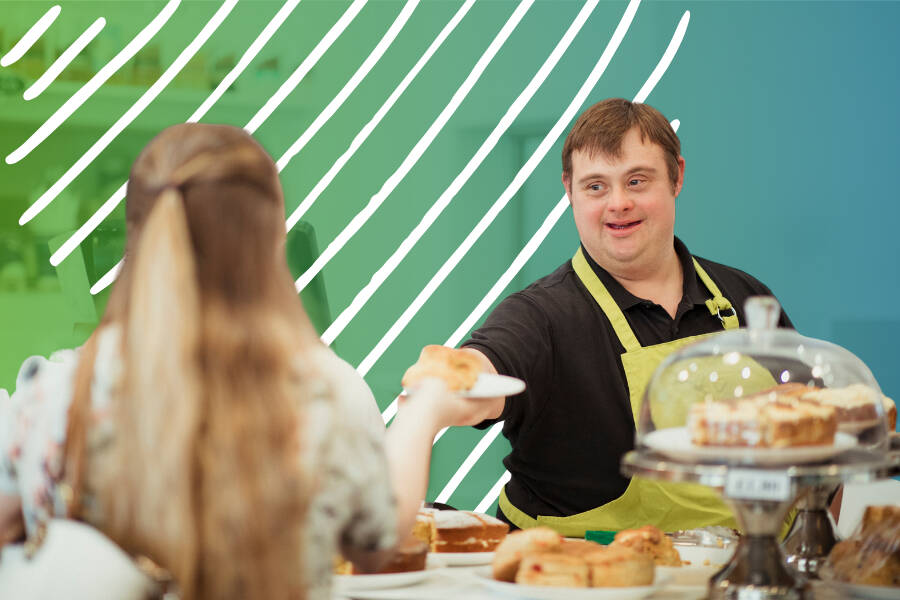 A bakery employee with Down syndrome, wearing a green apron, hands a plate of food to a customer across a café counter. Fresh baked goods and cakes are displayed in the foreground, while a green-to-blue graphic overlay with white curved lines.